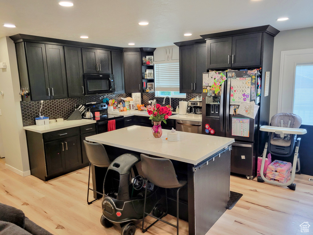 Kitchen featuring black appliances, light wood-type flooring, decorative backsplash, light countertops, and recessed lighting