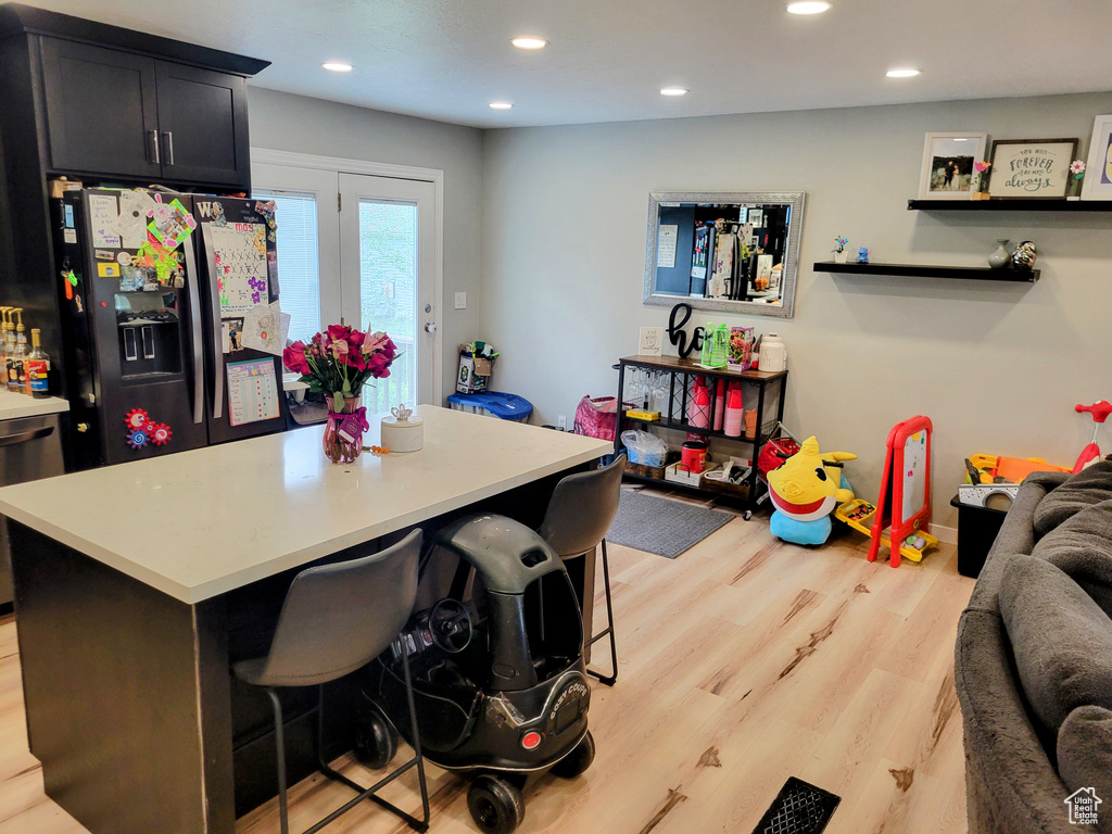 Kitchen with black refrigerator with ice dispenser, light wood-style floors, light countertops, a kitchen breakfast bar, and recessed lighting