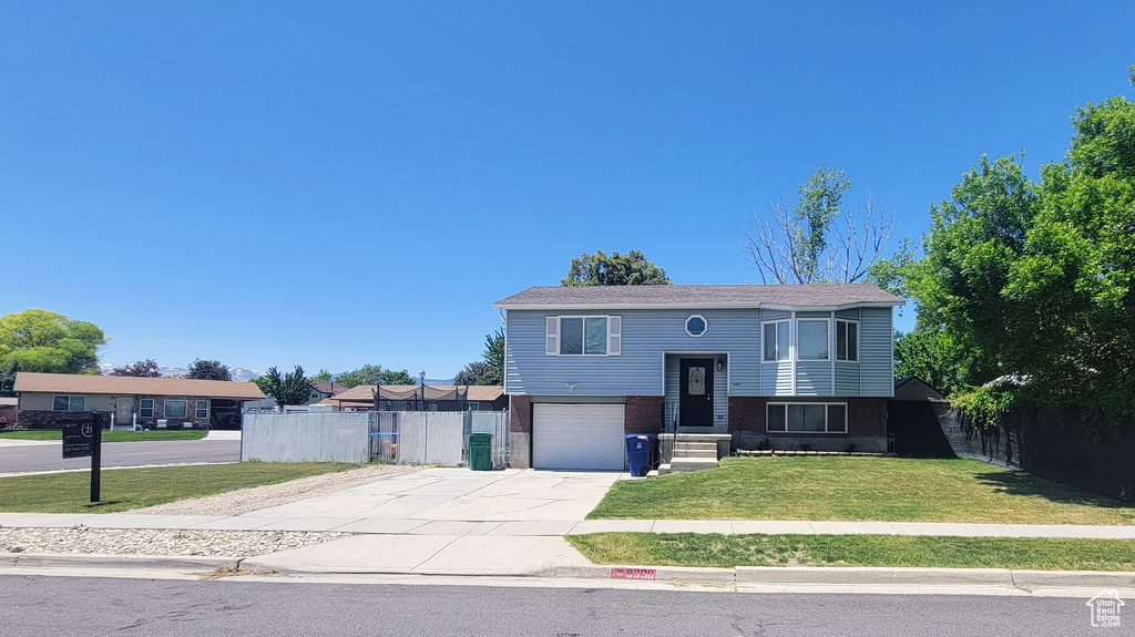 Raised ranch with concrete driveway, an attached garage, and brick siding