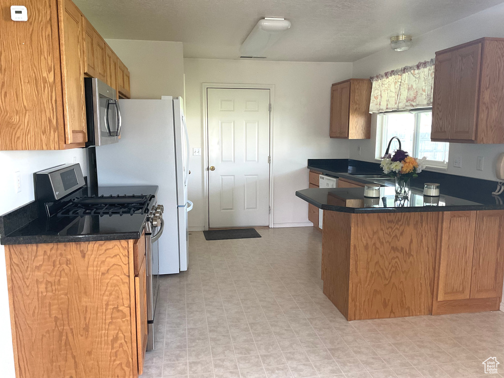 Kitchen featuring stainless steel appliances, dark countertops, a peninsula, and light flooring