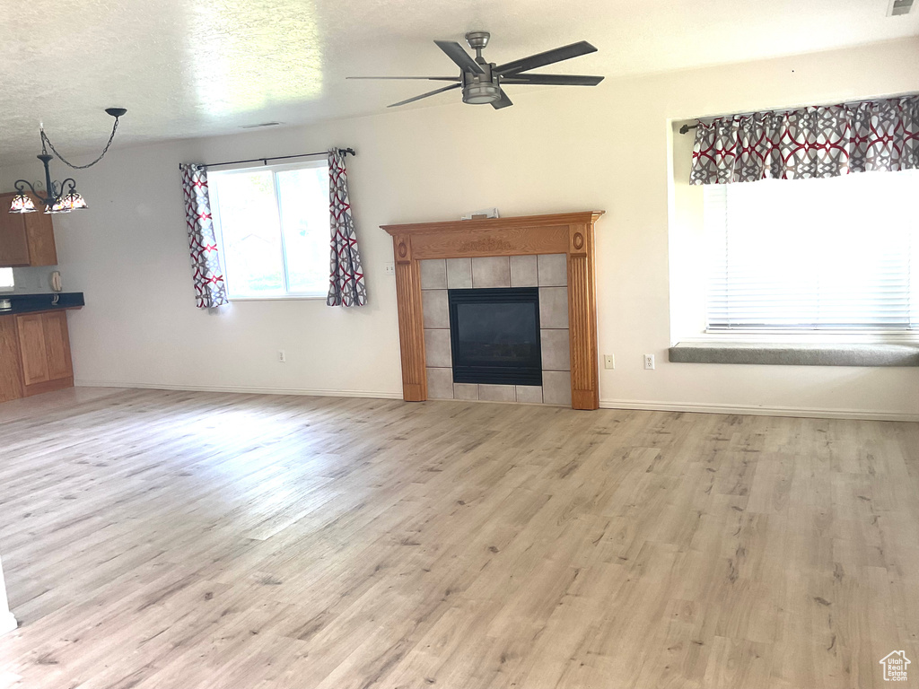 Unfurnished living room with light wood finished floors, ceiling fan, a fireplace, a chandelier, and baseboards