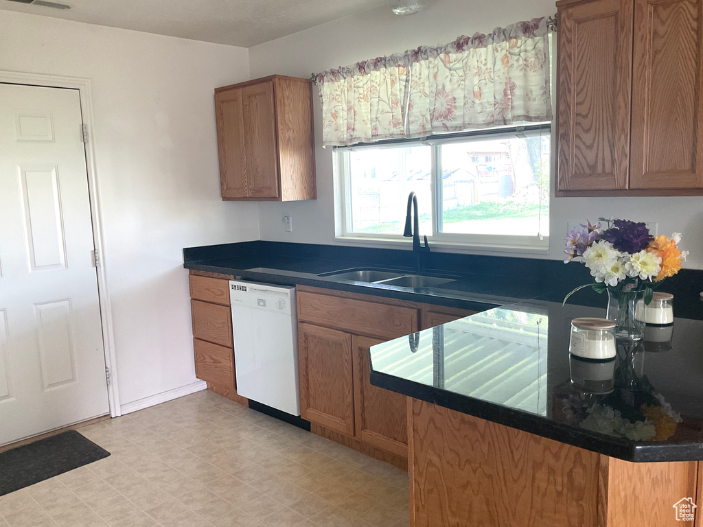Kitchen with dishwasher, a sink, brown cabinets, dark countertops, and light flooring