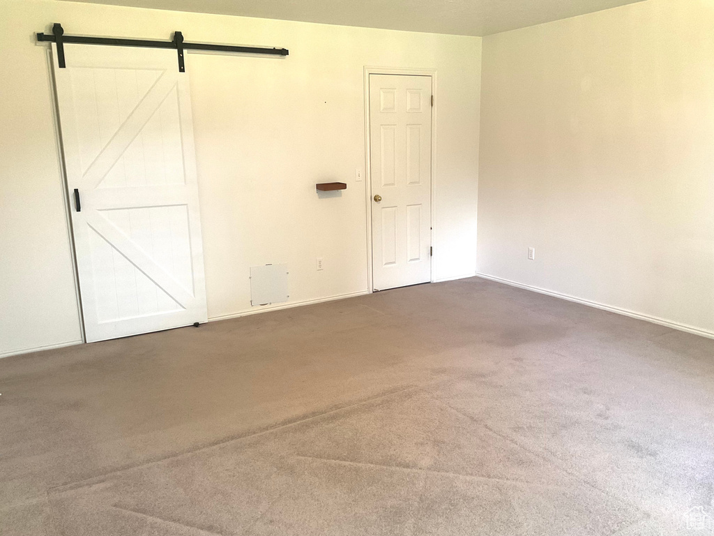 Unfurnished bedroom with carpet floors, baseboards, and a barn door