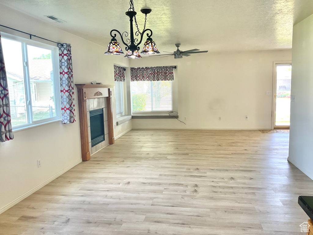 Unfurnished living room featuring healthy amount of natural light, light wood-style floors, a textured ceiling, and baseboards