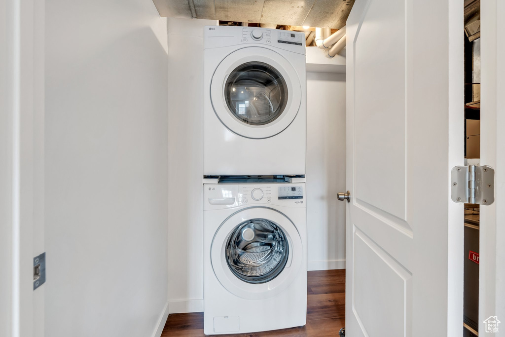 Washroom with stacked washer / dryer, wood finished floors, and baseboards