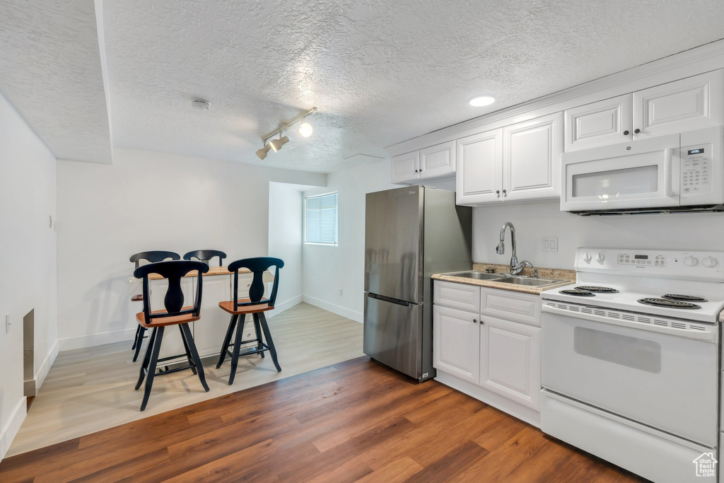 Kitchen with white appliances, a sink, wood finished floors, a textured ceiling, and white cabinetry