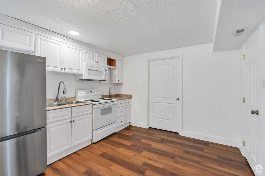 Kitchen with white appliances, a sink, dark wood-type flooring, baseboards, and white cabinetry