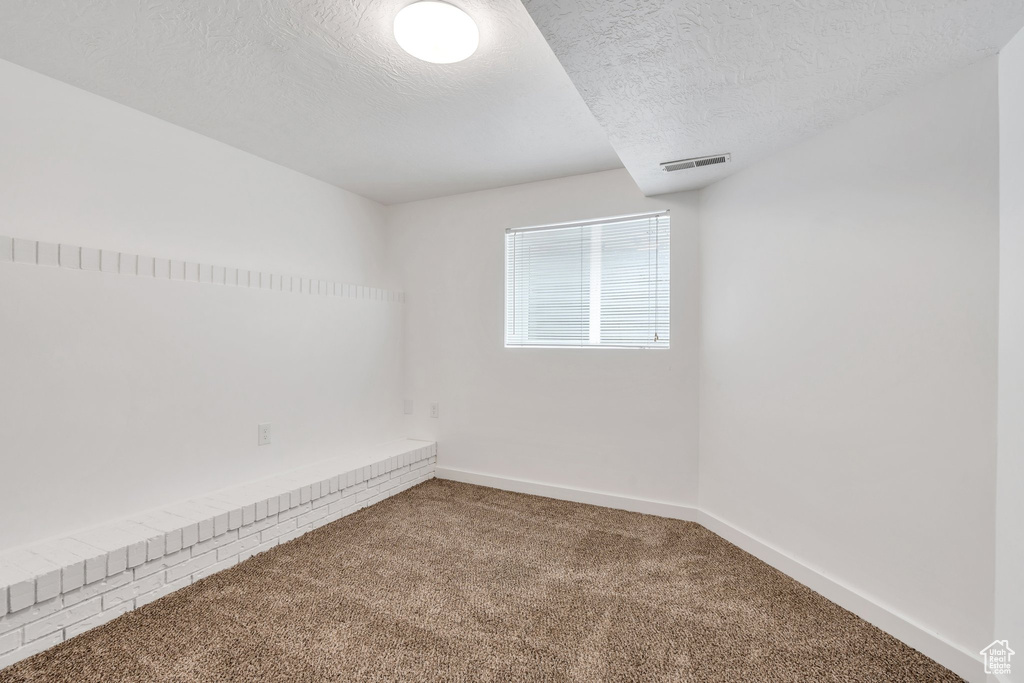 Empty room with carpet floors, baseboards, and a textured ceiling