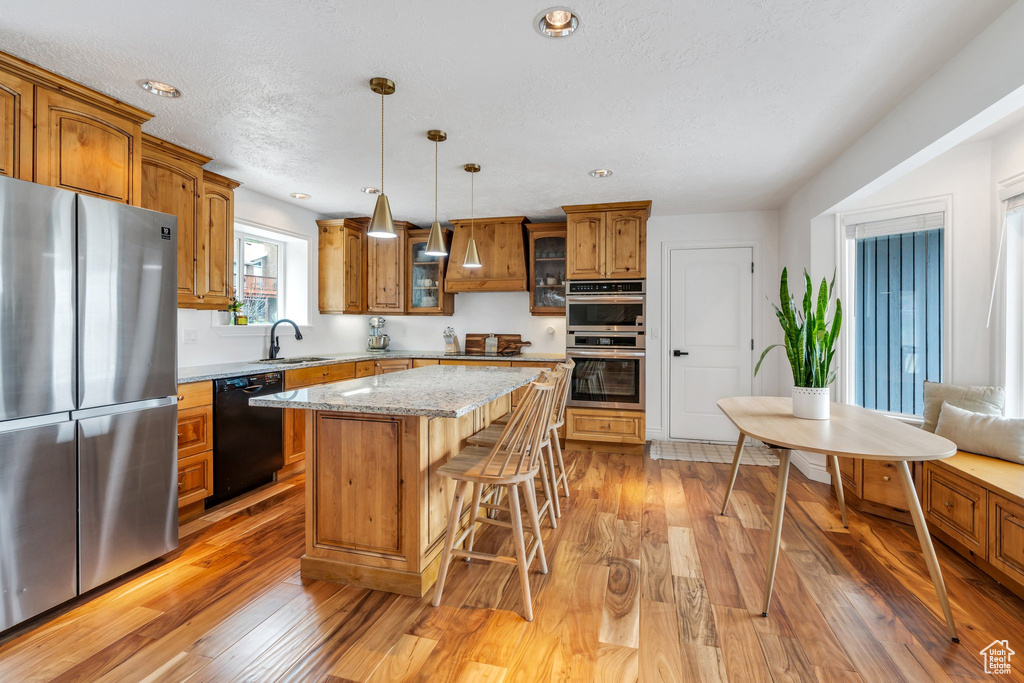 Kitchen with appliances with stainless steel finishes, brown cabinets, a breakfast bar, light wood finished floors, and recessed lighting