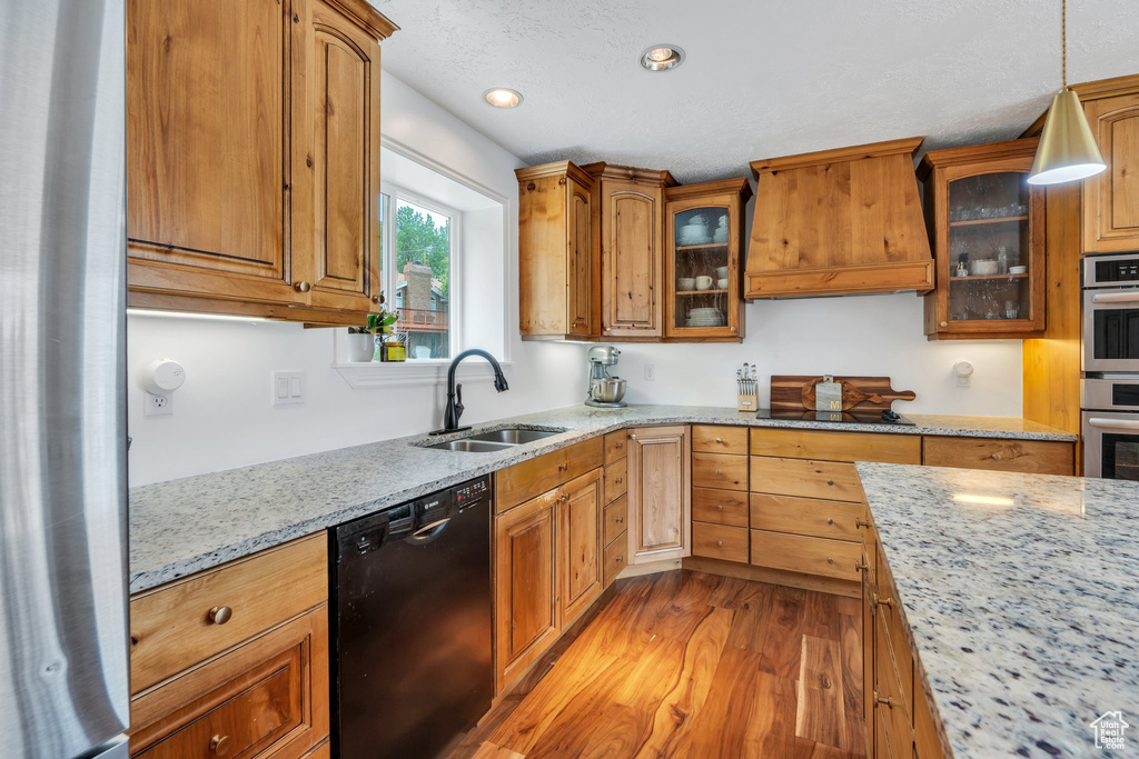 Kitchen with black appliances, premium range hood, a sink, light wood-type flooring, and light stone counters