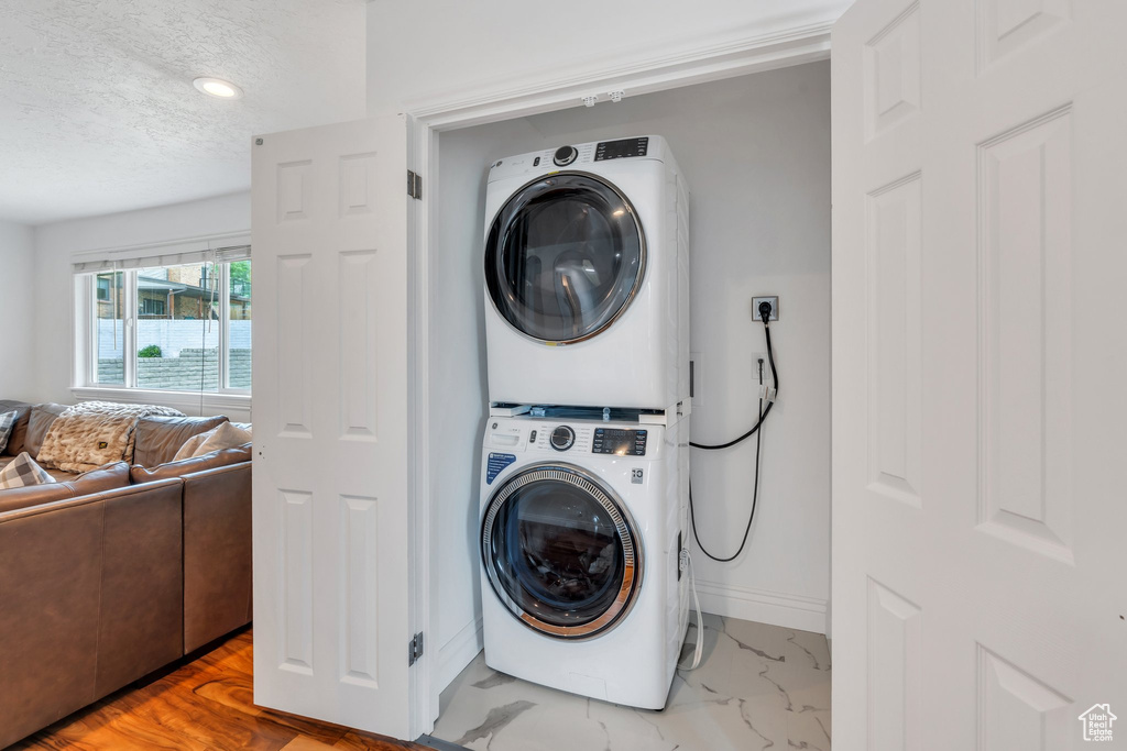 Washroom featuring estacked washer and dryer, a textured ceiling, baseboards, recessed lighting, and marble finish floors