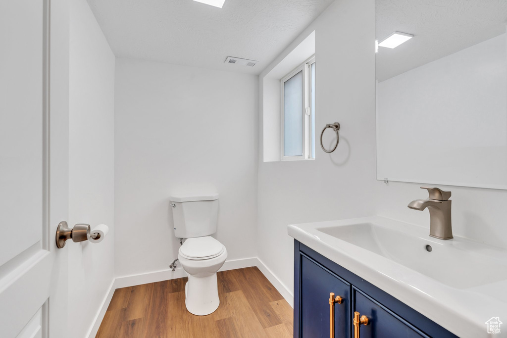 Half bathroom featuring wood finished floors, toilet, baseboards, and vanity