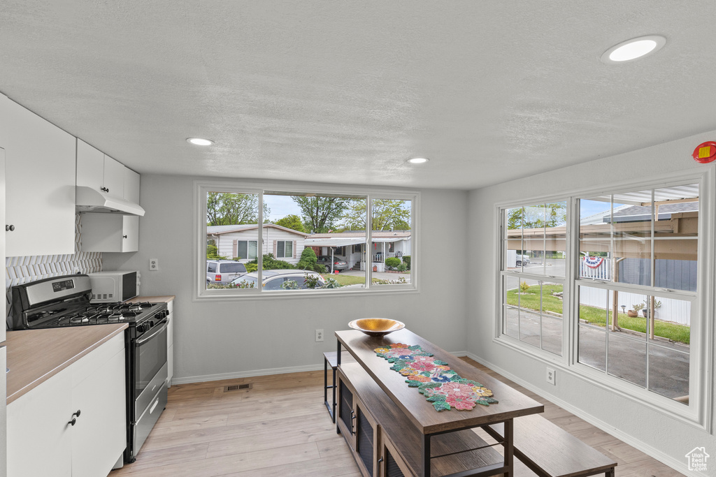 Kitchen featuring stainless steel range with gas cooktop, baseboards, healthy amount of natural light, white cabinetry, and a textured ceiling