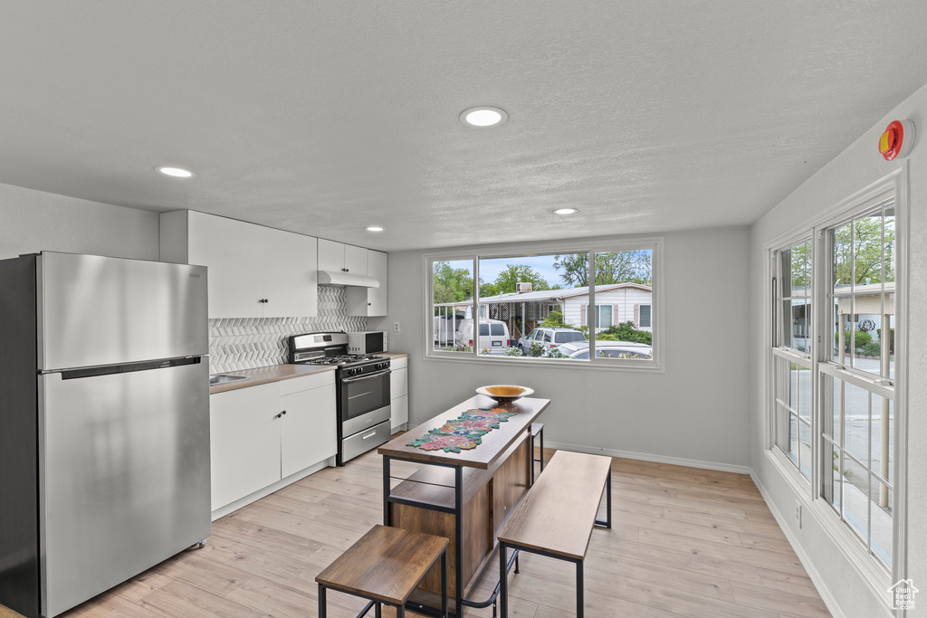 Kitchen featuring stainless steel appliances, white cabinetry, recessed lighting, light wood finished floors, and baseboards