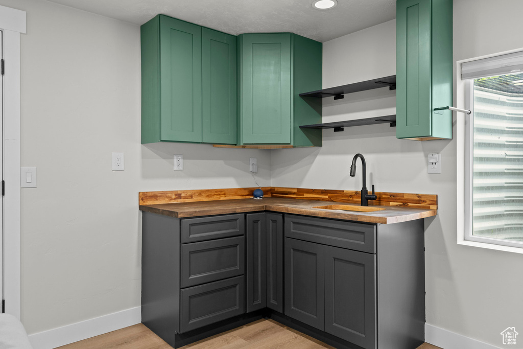 Kitchen featuring a sink, baseboards, light wood-type flooring, open shelves, and green cabinets