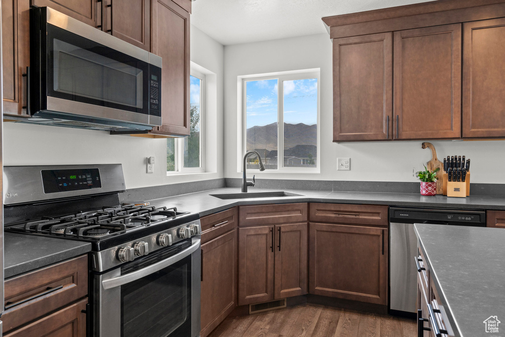 Kitchen with stainless steel appliances, a sink, dark countertops, wood finished floors, and a mountain view