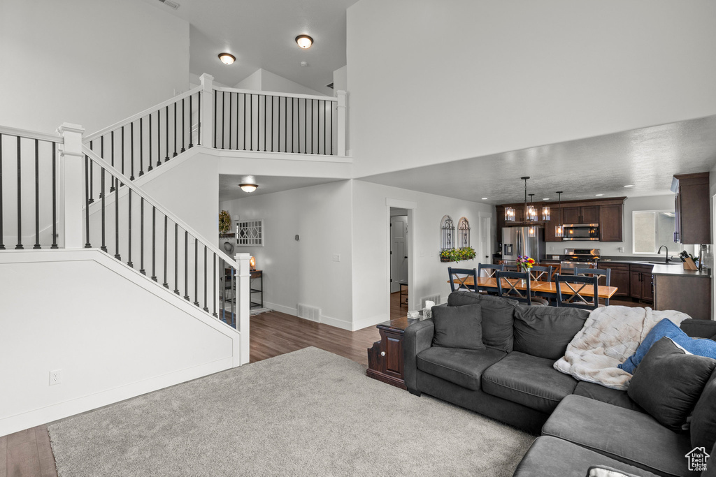 Living room featuring wood finished floors, stairs, a chandelier, a towering ceiling, and baseboards