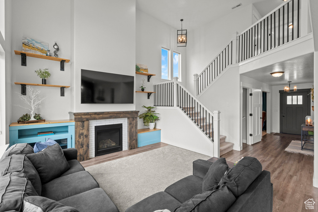 Living room featuring a towering ceiling, stairs, wood finished floors, a chandelier, and a fireplace