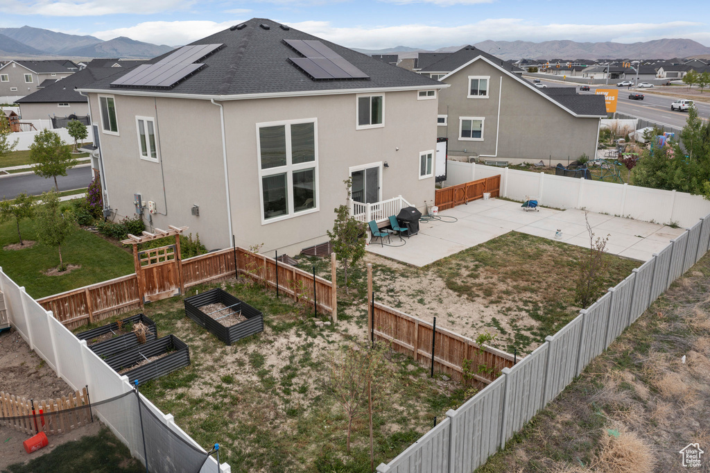 Back of house with a patio, a mountain view, stucco siding, roof mounted solar panels, and a garden