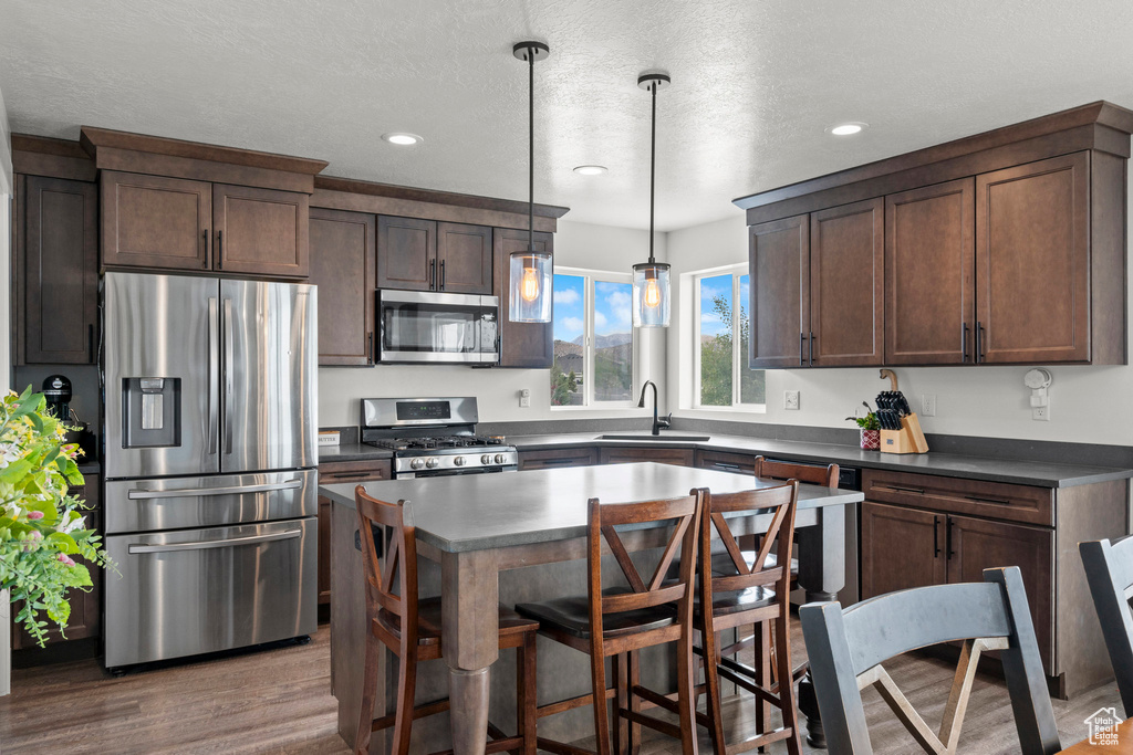 Kitchen featuring appliances with stainless steel finishes, wood finished floors, a sink, recessed lighting, and dark countertops