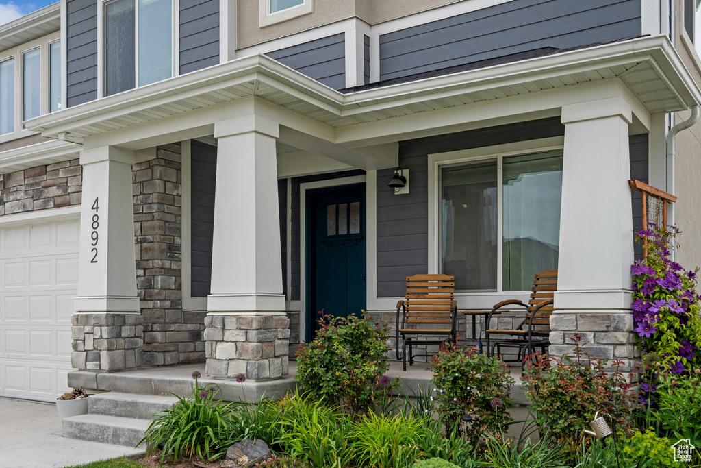 Entrance to property featuring a porch, stone siding, and an attached garage