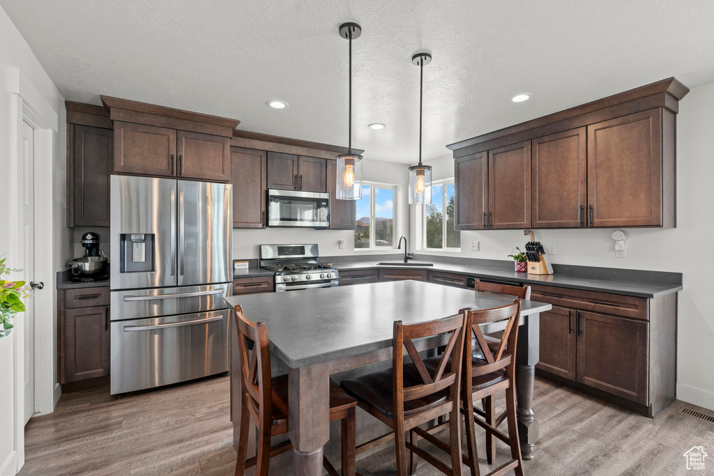 Kitchen with stainless steel appliances, dark countertops, light wood-style floors, a sink, and recessed lighting