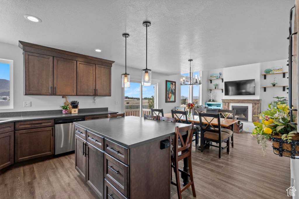 Kitchen with dishwasher, dark countertops, a breakfast bar area, wood finished floors, and a fireplace