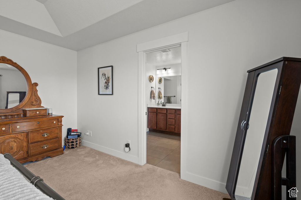 Tiled bedroom with carpet floors, baseboards, lofted ceiling, and ensuite bathroom