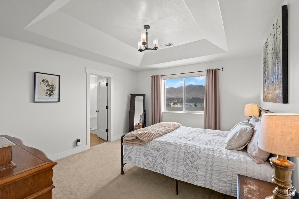 Carpeted bedroom with a raised ceiling, a chandelier, and baseboards