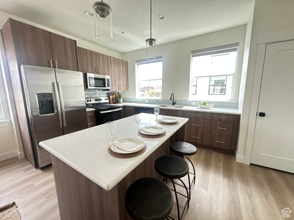 Kitchen with appliances with stainless steel finishes, a sink, light wood-style flooring, a kitchen bar, and light countertops