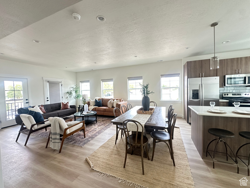 Dining area with light wood finished floors, a textured ceiling, healthy amount of natural light, and recessed lighting