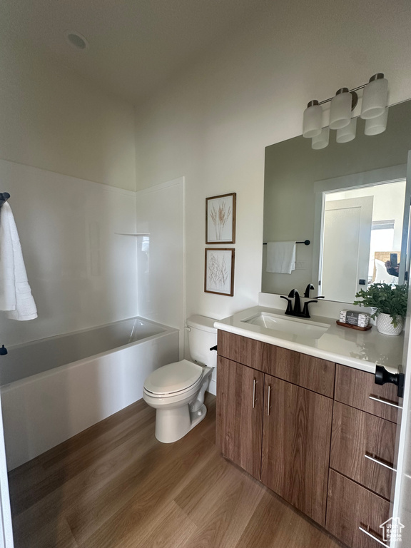 Bathroom with wood finished floors, toilet, vanity, and  shower combination