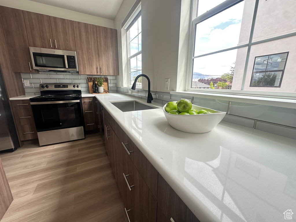 Kitchen with stainless steel appliances, a sink, light countertops, decorative backsplash, and light wood-type flooring