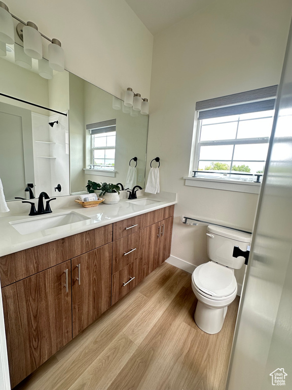 Full bathroom with wood finished floors, toilet, double vanity, and baseboards