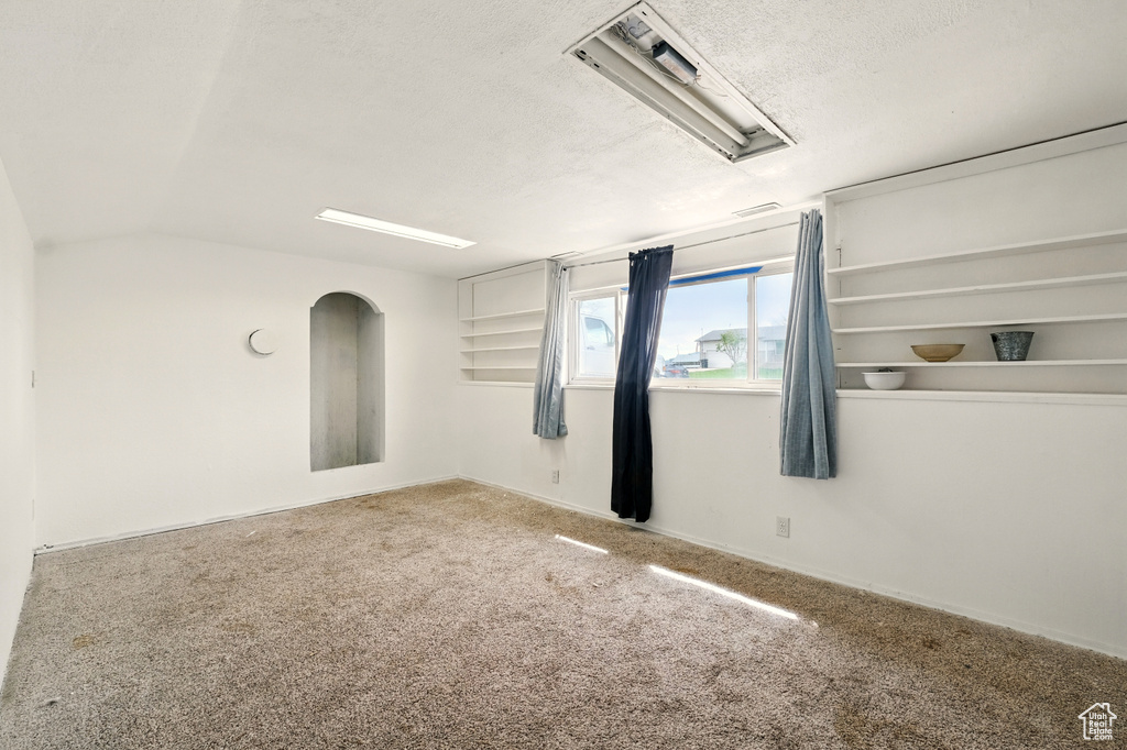 Carpeted spare room with a textured ceiling, baseboards, and vaulted ceiling