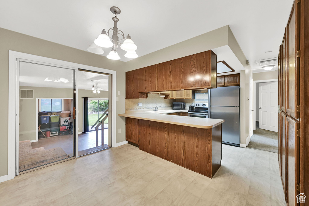 Kitchen with appliances with stainless steel finishes, light countertops, a peninsula, decorative backsplash, and a chandelier
