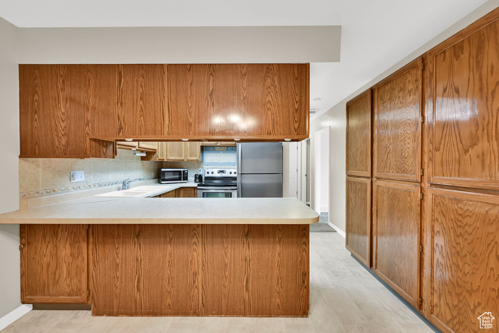 Kitchen featuring stainless steel appliances, a peninsula, light countertops, a sink, and brown cabinetry