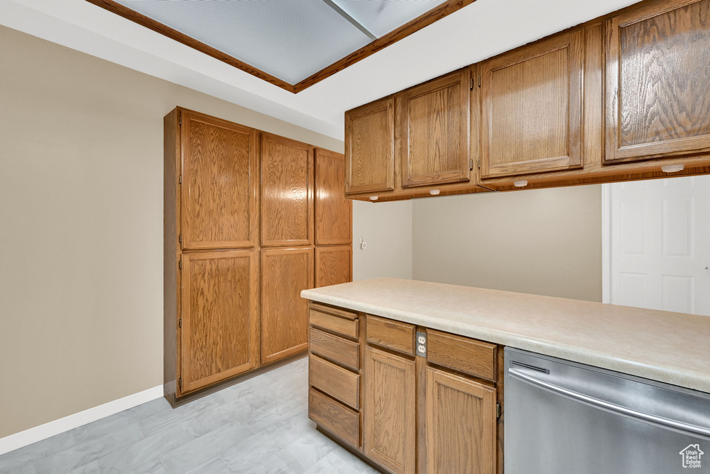Kitchen featuring stainless steel dishwasher, light countertops, brown cabinetry, and baseboards