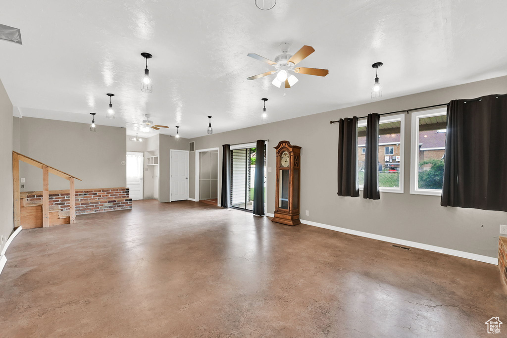 Unfurnished living room featuring ceiling fan, concrete flooring, and baseboards
