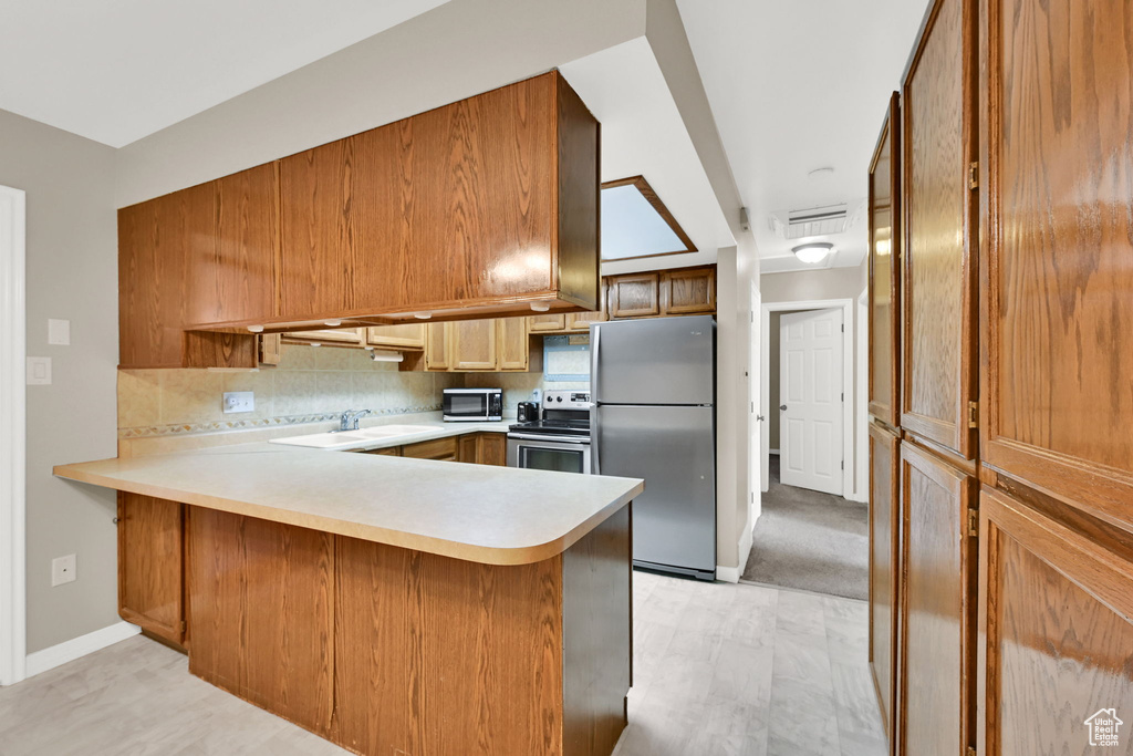 Kitchen with stainless steel appliances, light countertops, decorative backsplash, a peninsula, and a sink