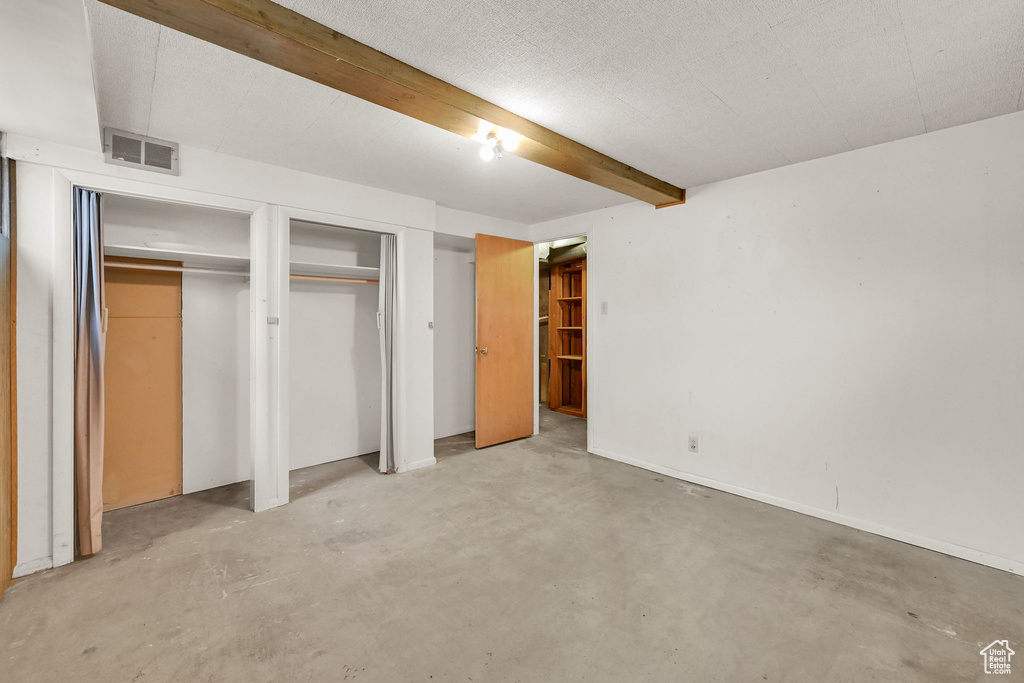Unfurnished bedroom with concrete flooring, beamed ceiling, and two closets