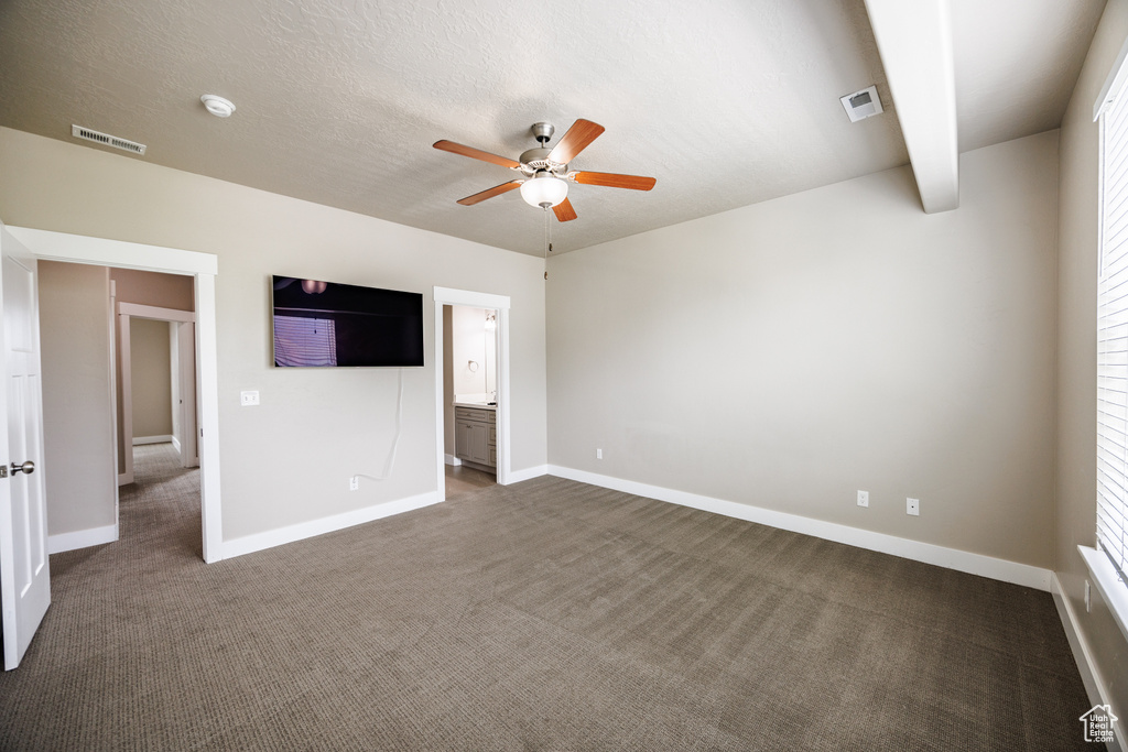 Unfurnished bedroom featuring dark carpet, baseboards, connected bathroom, and a ceiling fan