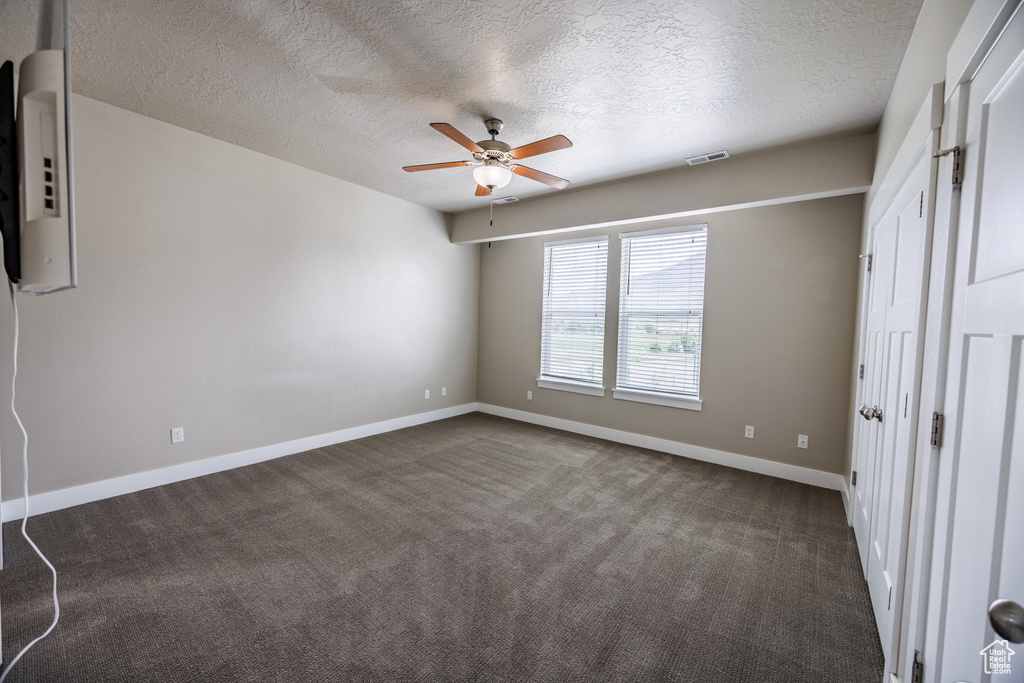 Unfurnished bedroom with dark carpet, a textured ceiling, baseboards, and a ceiling fan