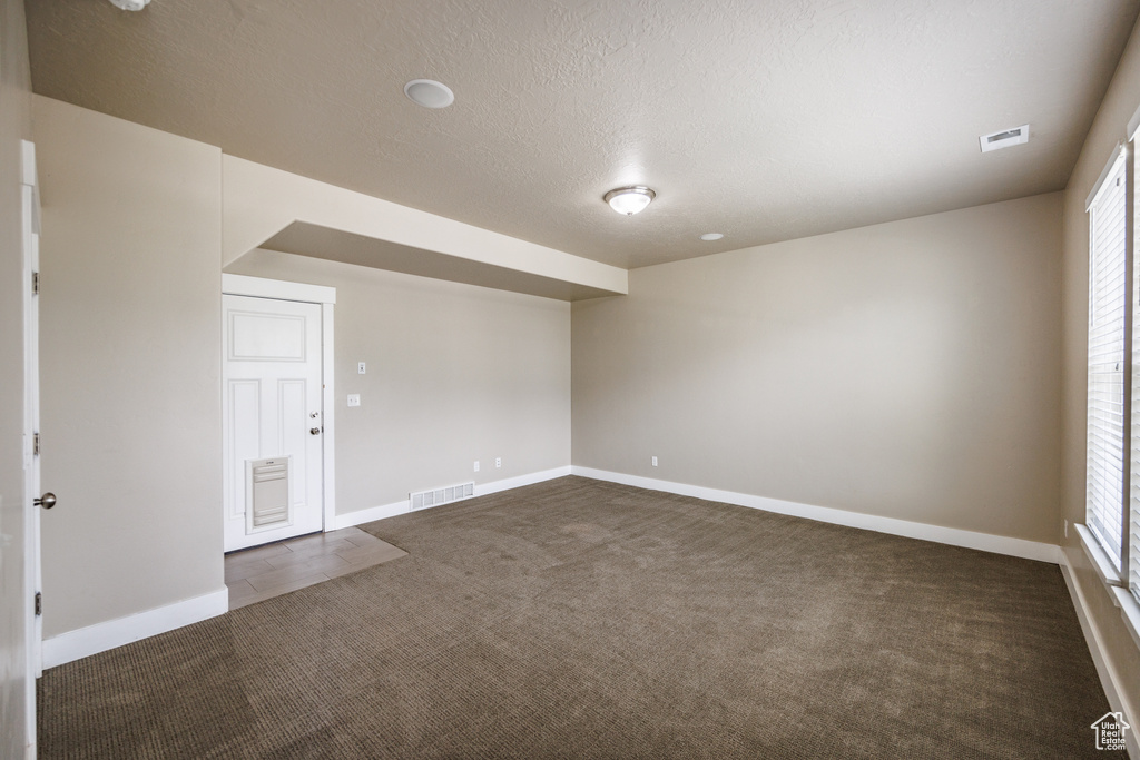 Empty room with dark colored carpet, a textured ceiling, and baseboards