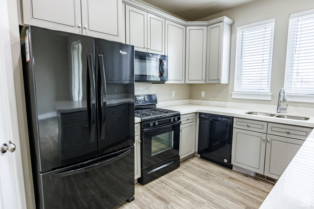 Kitchen featuring black appliances, a sink, light countertops, light wood-style floors, and gray cabinetry