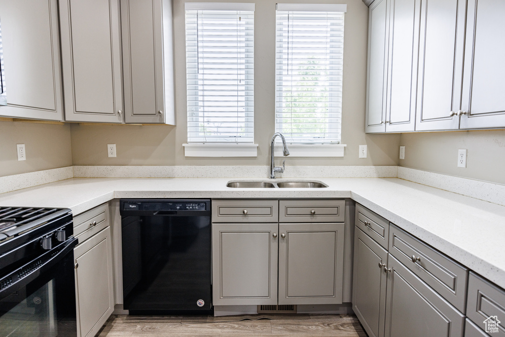 Kitchen with black appliances, a sink, gray cabinets, light countertops, and light wood-style flooring