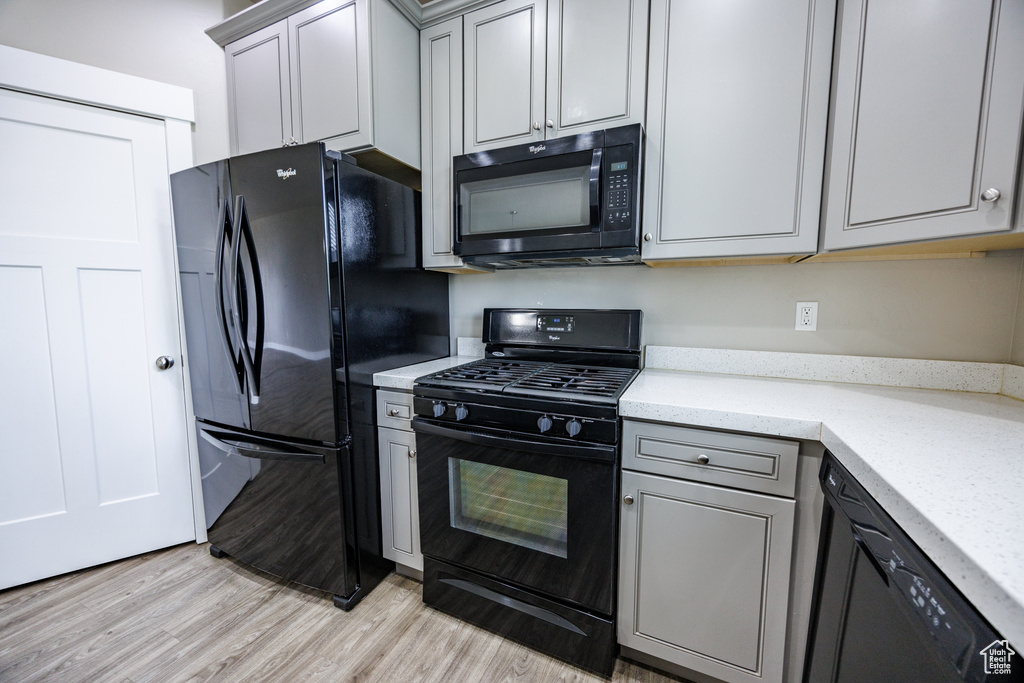 Kitchen featuring black appliances, light wood-type flooring, gray cabinetry, and light stone counters