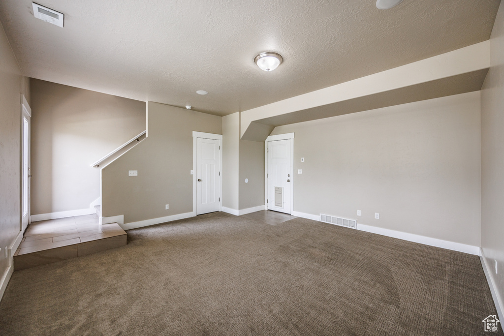 Unfurnished living room featuring carpet, baseboards, stairs, and a textured ceiling