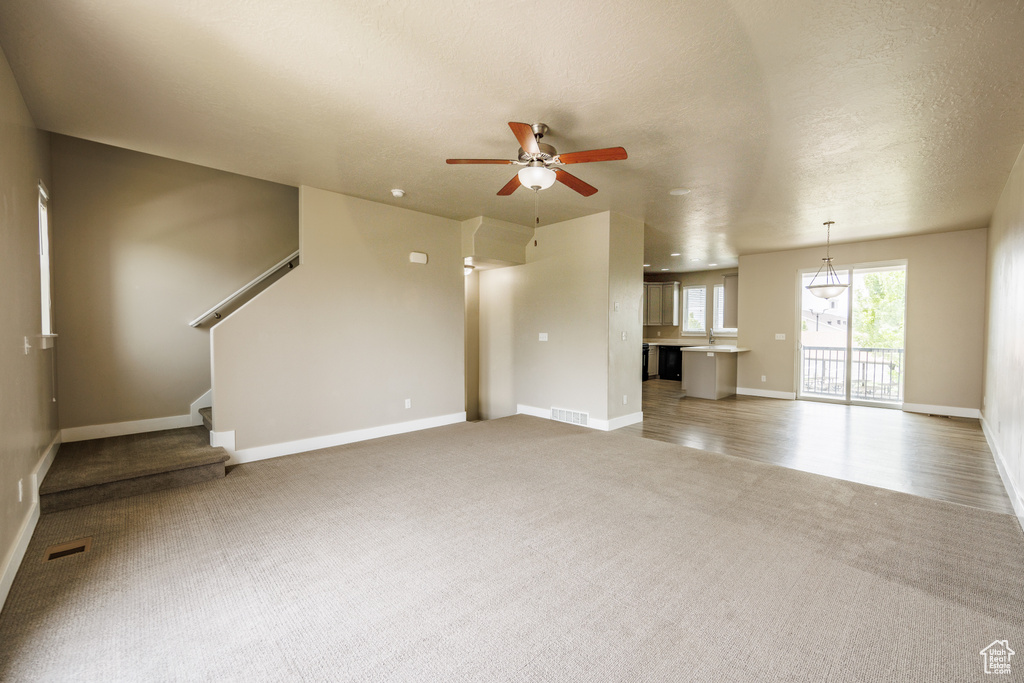 Unfurnished living room with light carpet, ceiling fan, baseboards, and stairway