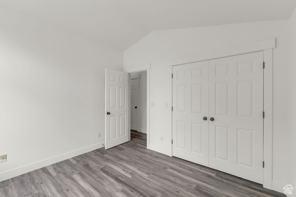 Unfurnished bedroom with lofted ceiling, wood finished floors, baseboards, and a closet